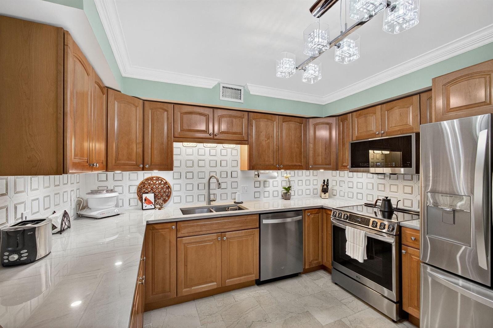 A kitchen with wood cabinets, stainless steel appliances, white countertops, and a tiled backsplash — 129 S Golfview Road # 7, FL 33460, FL