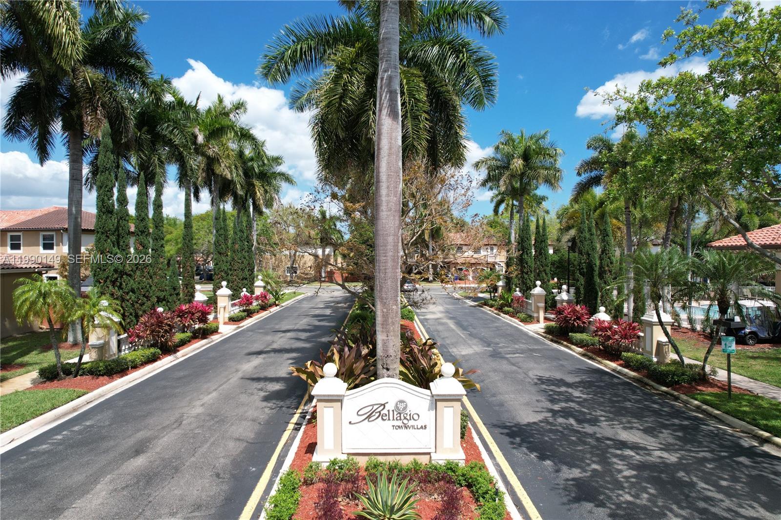 A palm-lined entrance road leads to a sign for Bellagio Townvillas under a blue sky — 4964 SW 128th Ave, Miramar FL 33027, MIRAMAR, FL