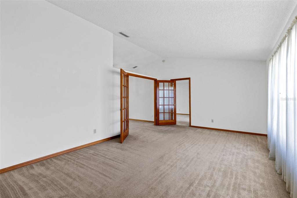 An empty room with beige carpet, white walls, and wooden French doors leading to another space — 602 VICKSBURG STREET, DELTONA, FL