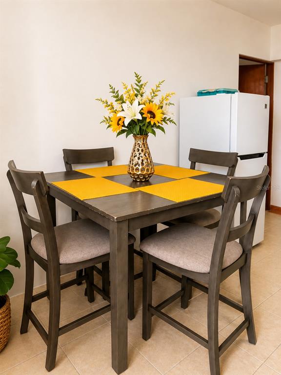 A square dining table with four chairs and a floral centerpiece sits near a refrigerator — CII Via 2 VILLA FONTANA, CAROLINA, PR