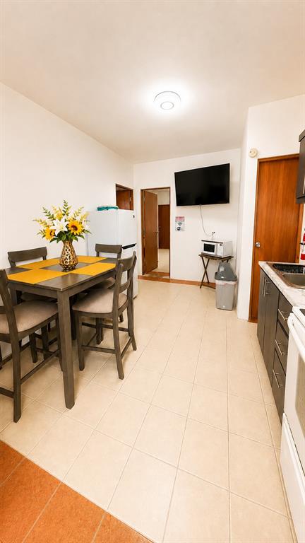 A kitchen and dining area with tile floors, a wooden table, and a wall-mounted television — CII Via 2 VILLA FONTANA, CAROLINA, PR