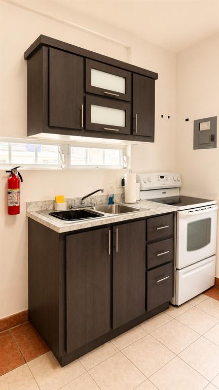 A kitchen features dark wood cabinets, a stainless steel sink, and a white electric stove — CII Via 2 VILLA FONTANA, CAROLINA, PR