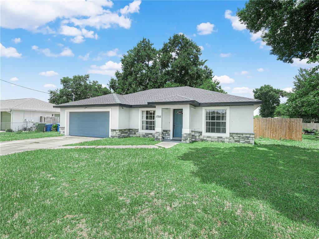 A single-story house with a blue garage door, white stucco walls, and stone accents — 1705 SANDALWOOD CIRCLE SW, WINTER HAVEN, FL