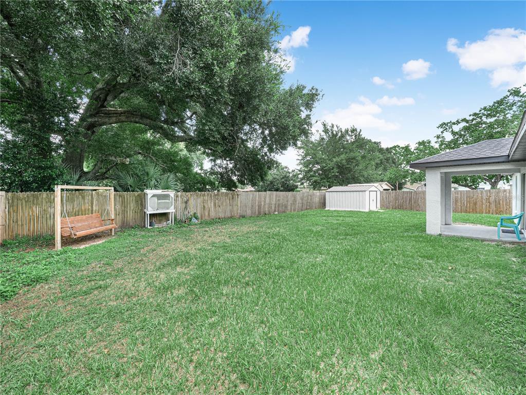 A grassy backyard features a wooden swing, a metal shed, and a covered patio area — 1705 SANDALWOOD CIRCLE SW, WINTER HAVEN, FL