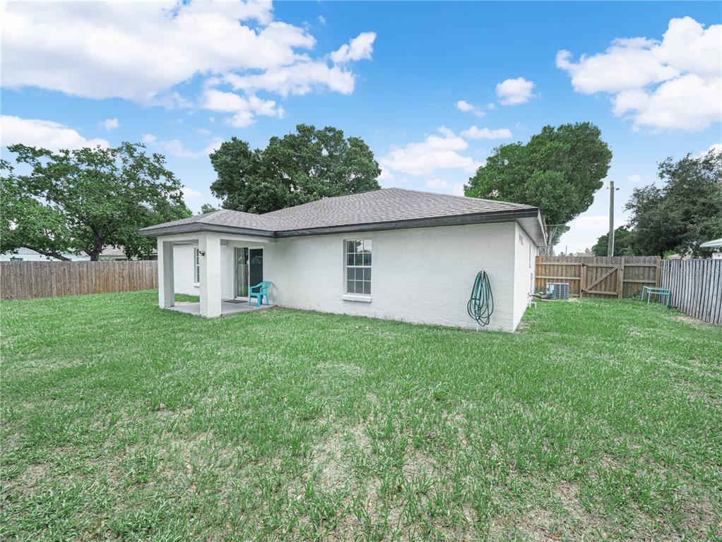The exterior of a white stucco house features a small covered patio and a grassy backyard — 1705 SANDALWOOD CIRCLE SW, WINTER HAVEN, FL