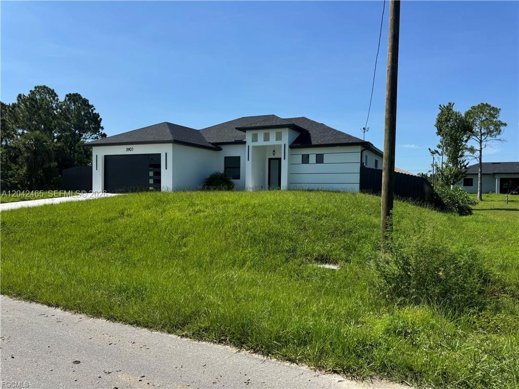 A modern, single-story house with a white exterior and dark roof sits on a grassy lot — 3901 3rd ST SW, Lehigh Acres FL 33976, LEHIGH ACRES, FL