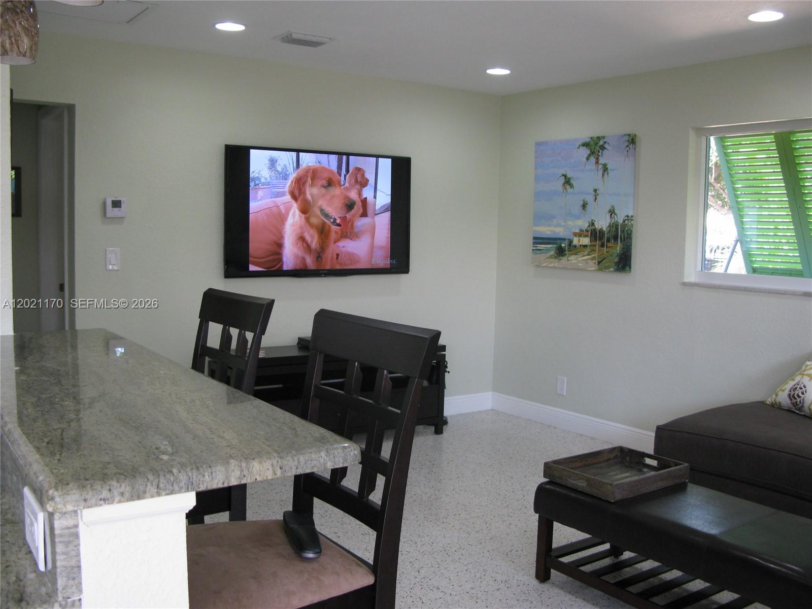 A living room features a wall-mounted television, a granite breakfast bar, and a window — 13767 Oleander Ave, Juno Beach FL 33408, JUNO BEACH, FL