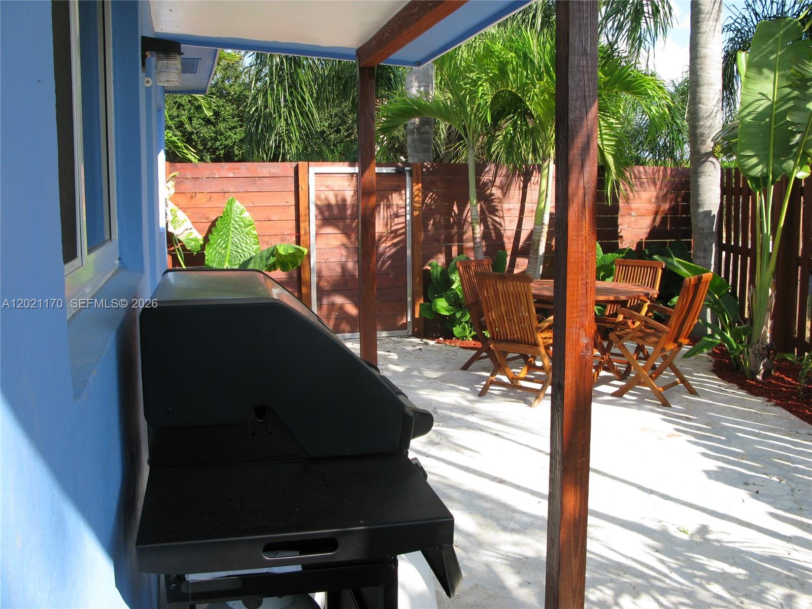 A patio features a grill, wooden dining furniture, and a fence under a covered area — 13767 Oleander Ave, Juno Beach FL 33408, JUNO BEACH, FL