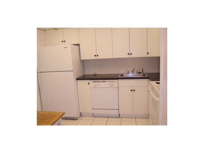A kitchen with white cabinets, white appliances, a dark countertop, and tiled flooring — 4158 Inverrary Drive # 404, Lauderhill FL 33319, LAUDERHILL, FL