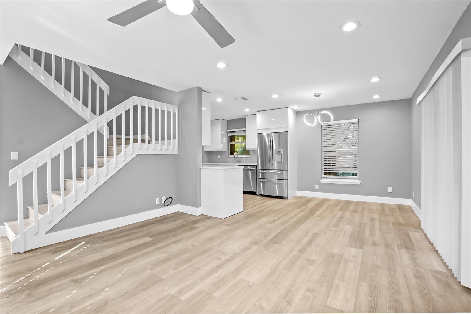 An open-concept living area features light wood flooring, a white staircase, and a modern kitchen — 17376 Sentimental Journey, Jupiter FL 33458, JUPITER, FL