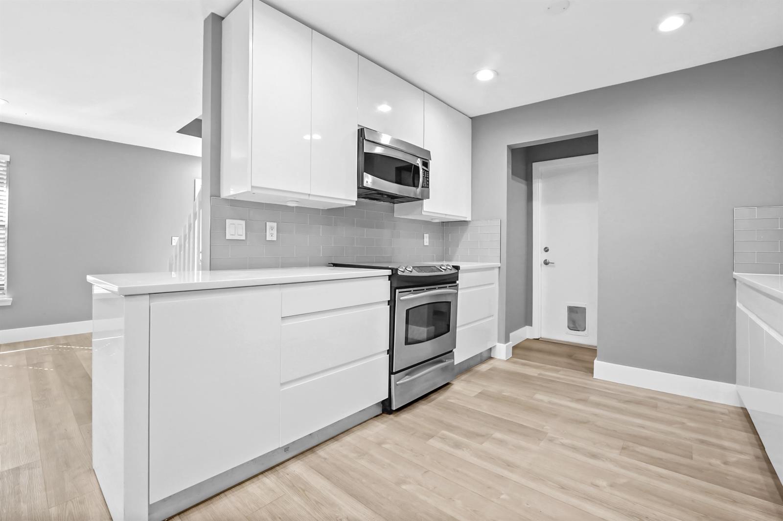 A modern kitchen features white flat-panel cabinets, stainless steel appliances, and light wood-look flooring — 17376 Sentimental Journey, Jupiter FL 33458, JUPITER, FL