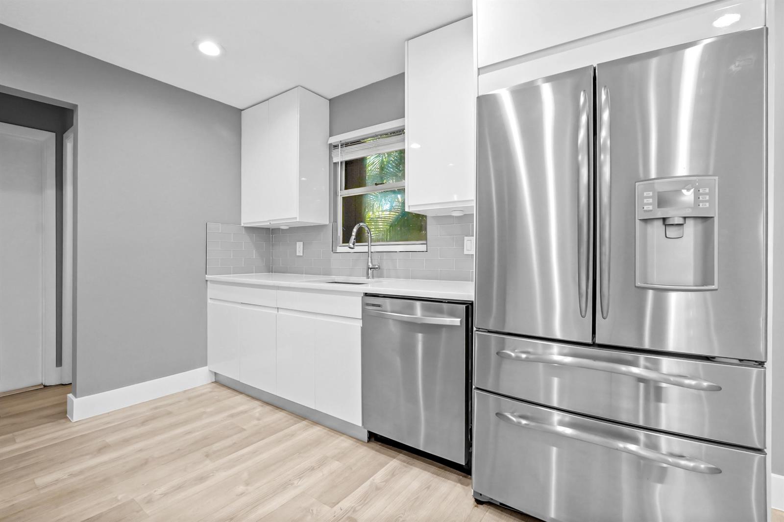 A modern kitchen features white cabinets, stainless steel appliances, gray subway tile, and light flooring — 17376 Sentimental Journey, Jupiter FL 33458, JUPITER, FL