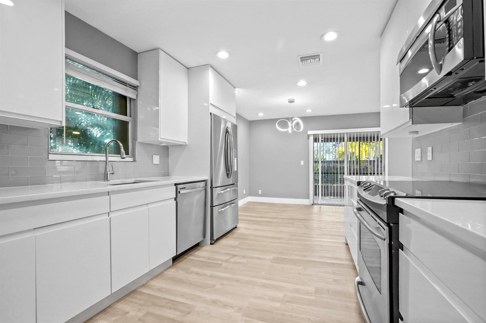 A modern kitchen features white cabinets, stainless steel appliances, gray tile backsplash, and light wood flooring — 17376 Sentimental Journey, Jupiter FL 33458, JUPITER, FL