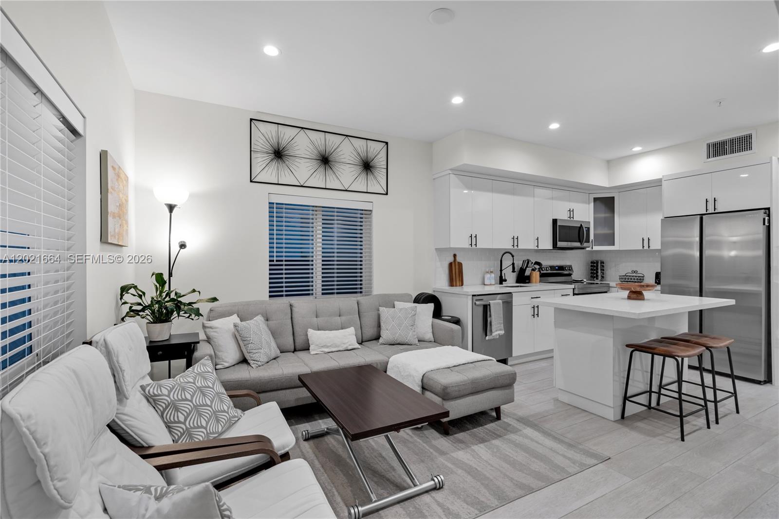 A modern open-concept living room and kitchen featuring white cabinetry, stainless steel appliances, and gray furniture — 1786 SW 9th St # 1, Miami FL 33135, MIAMI, FL