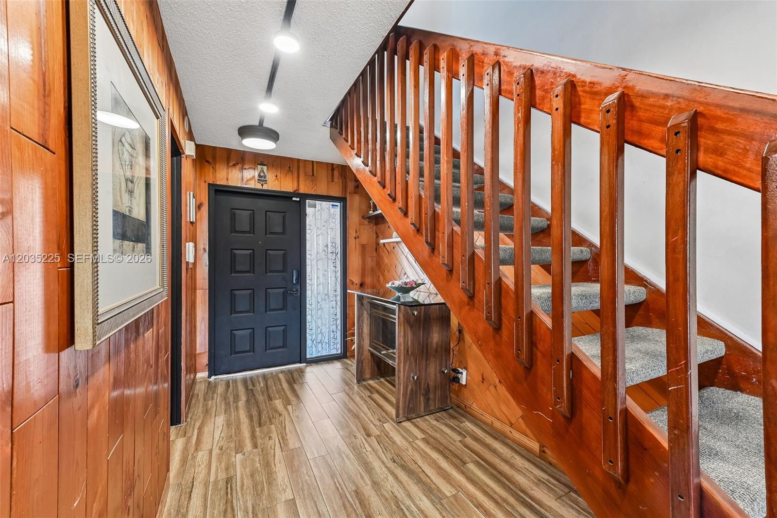 An entryway features wood-paneled walls, a black front door, and a wooden staircase with carpet — 207 NW 45th Ave, Deerfield Beach FL 33442, DEERFIELD BEACH, FL