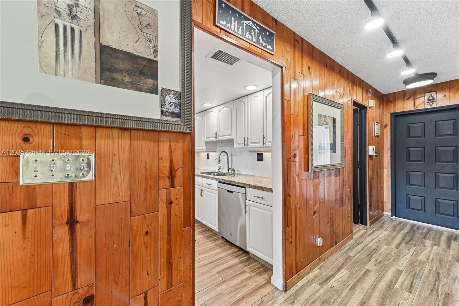 A hallway with wood-paneled walls leads to a kitchen featuring white cabinets and stainless appliances — 207 NW 45th Ave, Deerfield Beach FL 33442, DEERFIELD BEACH, FL