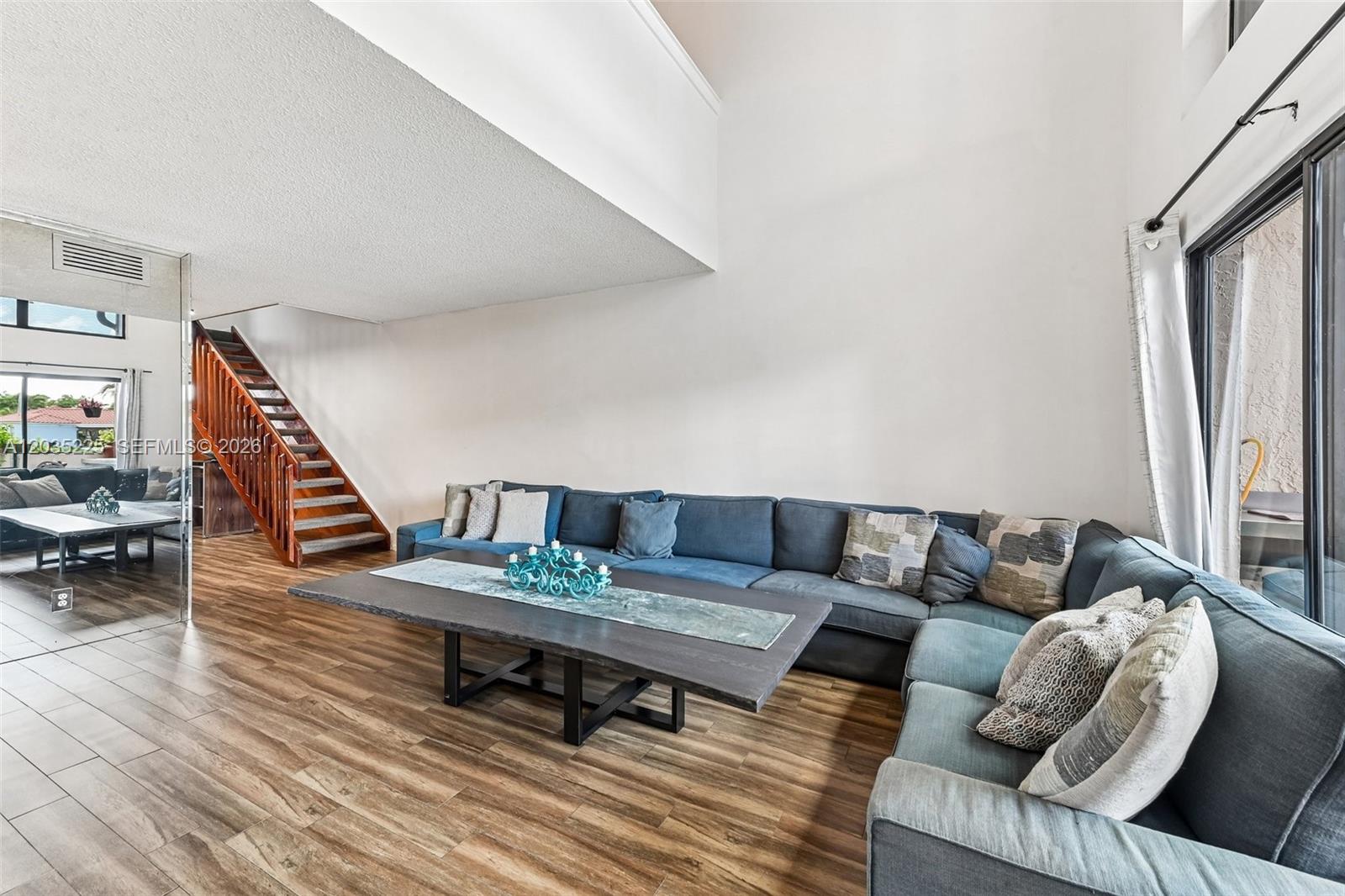 A living room features a large blue sectional sofa, a wooden coffee table, and stairs — 207 NW 45th Ave, Deerfield Beach FL 33442, DEERFIELD BEACH, FL