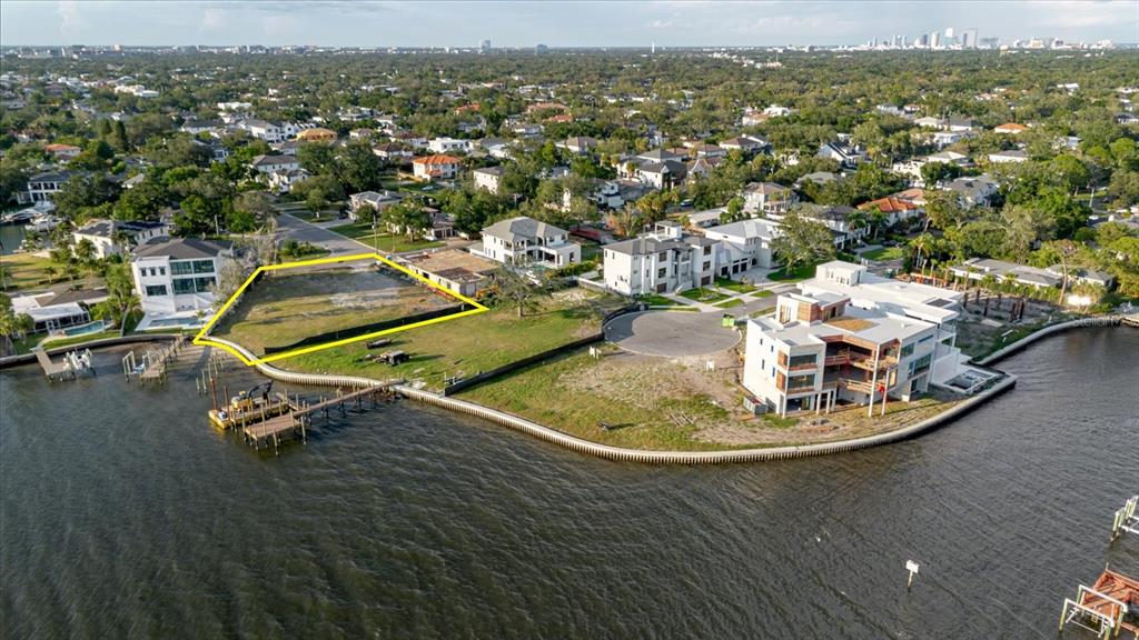 An aerial view shows a vacant waterfront lot outlined in yellow next to modern homes — 5102 W LONGFELLOW AVENUE, TAMPA, FL