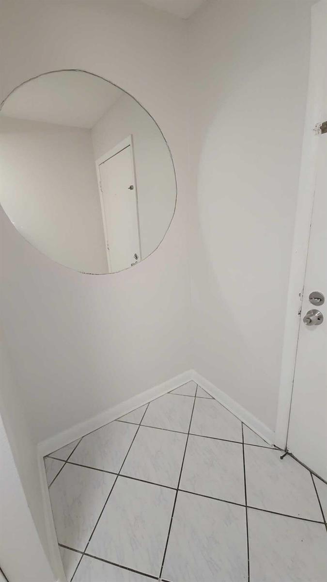 A small entryway features white walls, a large circular mirror, and white diagonal floor tiles — 4111 Stirling Road # 406, Dania Beach FL 33314, DANIA BEACH, FL
