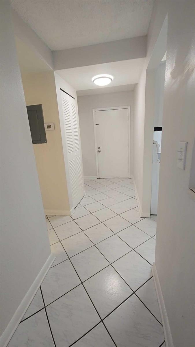 A hallway with white walls, white tile flooring, and a white door at the end — 4111 Stirling Road # 406, Dania Beach FL 33314, DANIA BEACH, FL