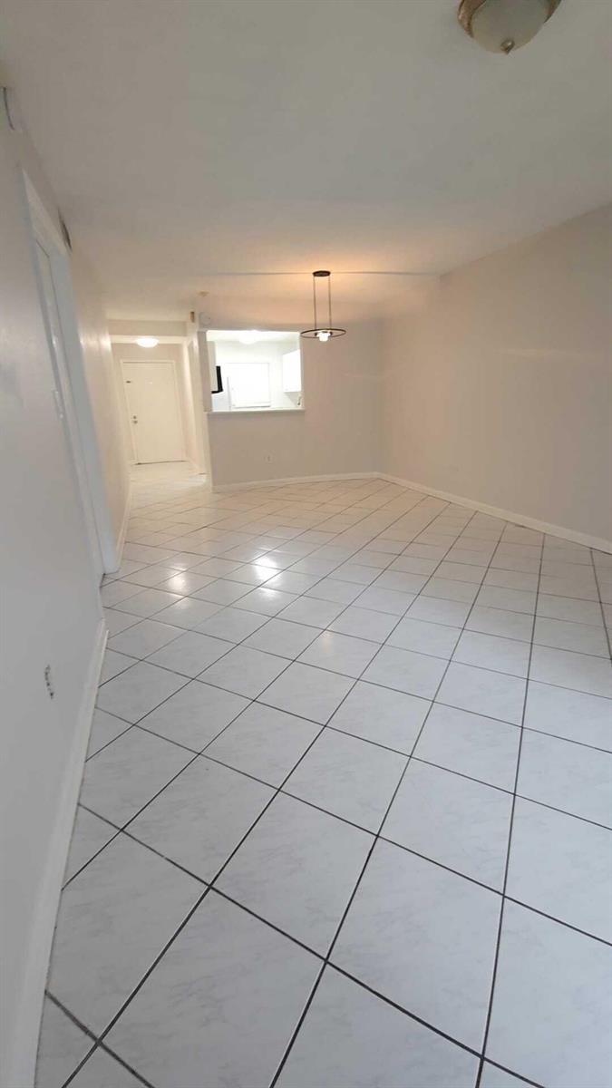 An empty room with white tile flooring, a pass-through window, and a hanging light fixture — 4111 Stirling Road # 406, Dania Beach FL 33314, DANIA BEACH, FL