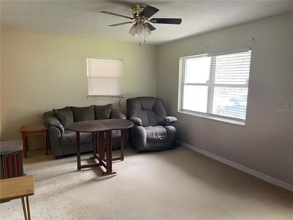 A living room features a sofa, recliner, folding table, ceiling fan, and carpeted flooring — 2209 NE 36TH STREET, OCALA, FL