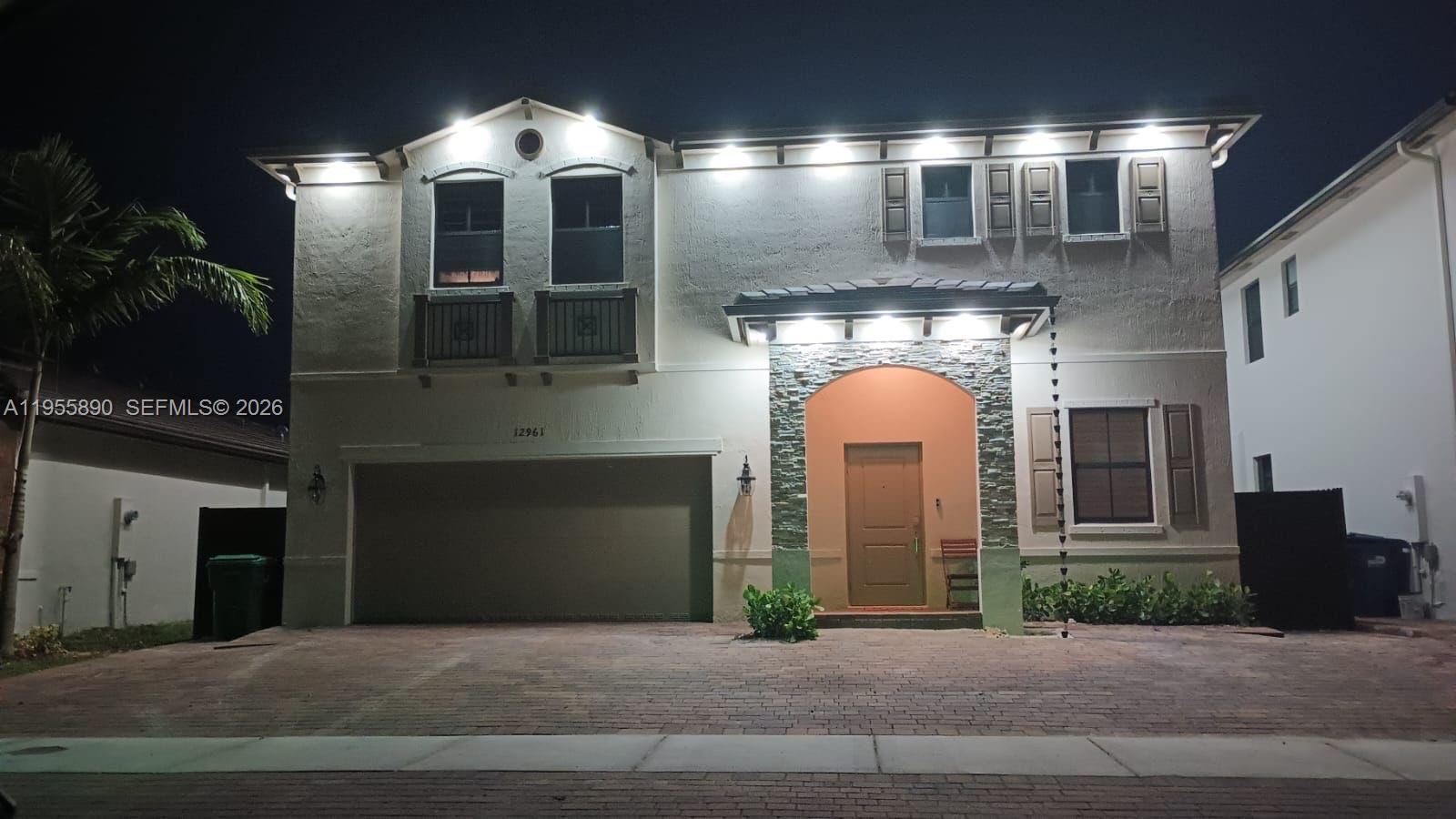 A two-story house exterior at night features a stone-accented entryway and a paved driveway — 12961 SW 230th St, Miami FL 33170, MIAMI, FL
