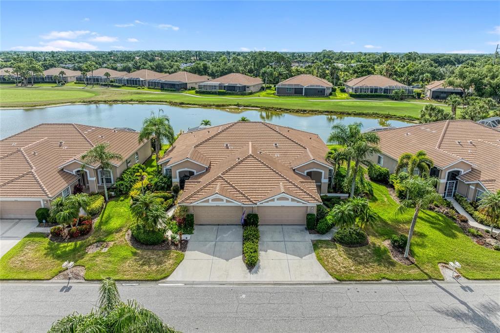An aerial view shows a duplex home with a tiled roof facing a pond — 9532 FOREST HILLS CIRCLE, SARASOTA, FL