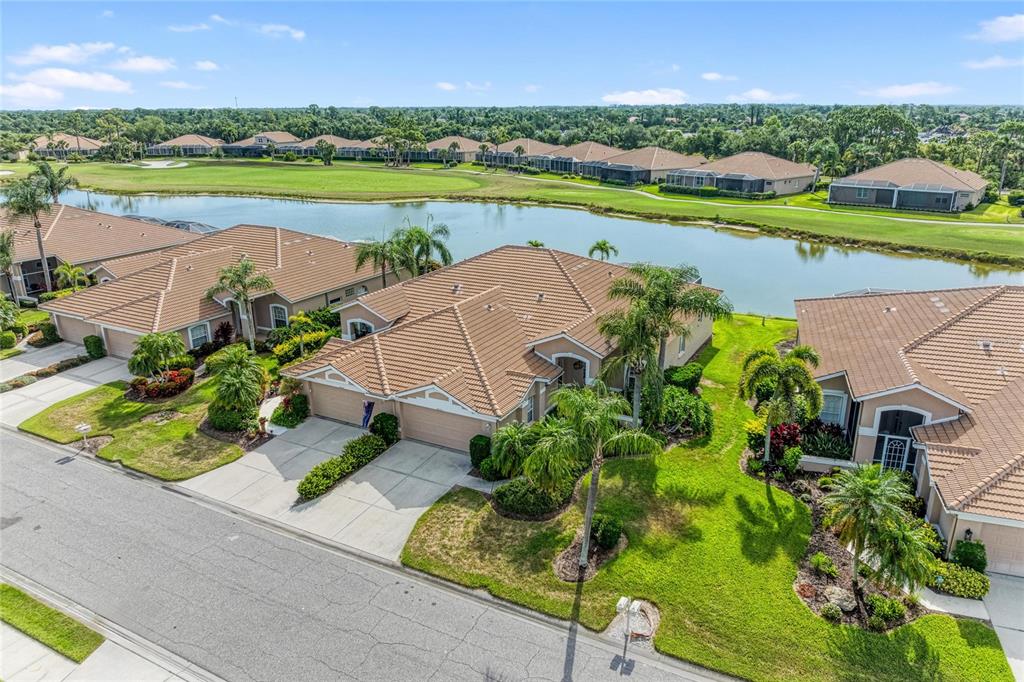 An aerial view shows suburban houses with tile roofs situated along a golf course pond — 9532 FOREST HILLS CIRCLE, SARASOTA, FL