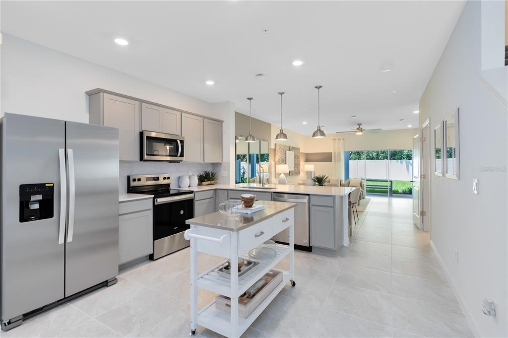 A modern kitchen features gray cabinets, stainless steel appliances, a white rolling island, and tile flooring — 4975 SUNRISE ESTATES DRIVE, WEST MELBOURNE, FL