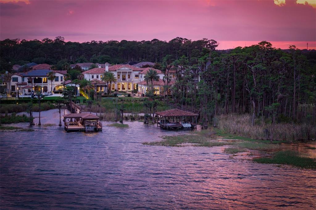 An aerial view of a large waterfront mansion with two boat docks at sunset — 6119 GROSVENOR SHORE DRIVE, WINDERMERE, FL