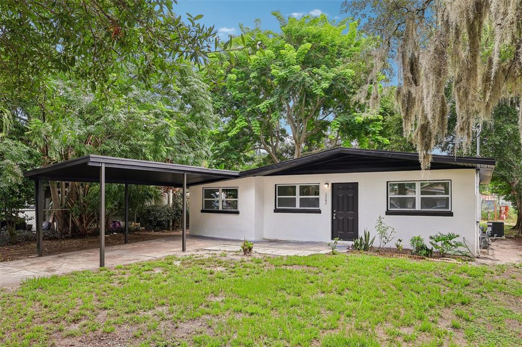 A single-story white house with a black roof, a carport, and a front lawn — 1207 32ND STREET NW, WINTER HAVEN, FL