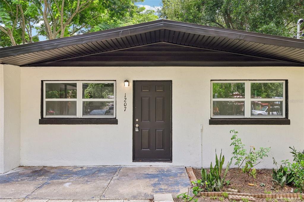 The exterior of a single-story home features a dark door, two windows, and a roof overhang — 1207 32ND STREET NW, WINTER HAVEN, FL
