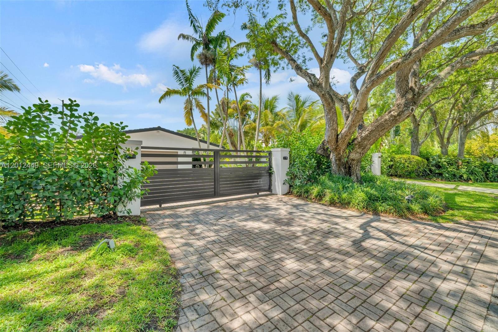 A paved driveway leads to a gated entrance in front of a house with landscaping — 6200 SW 118th St, Pinecrest FL 33156, PINECREST, FL