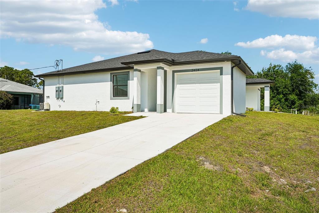 A single-story white house with a gray roof, a garage, and a concrete driveway — 2406 HIGHTOWER AVENUE S, LEHIGH ACRES, FL