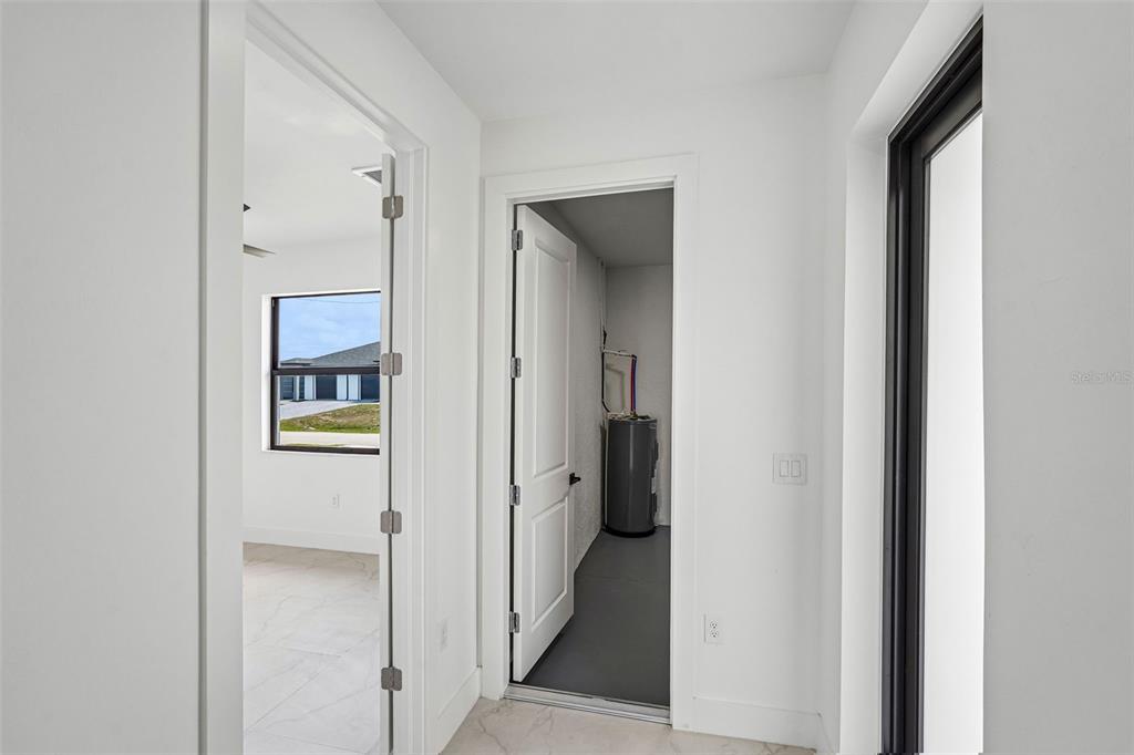 A hallway with white walls and tile floors leads to a utility closet and bedroom — 2406 HIGHTOWER AVENUE S, LEHIGH ACRES, FL