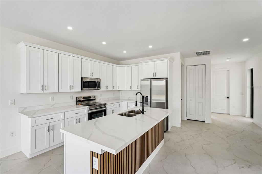 A modern kitchen features white cabinets, a marble-topped island with wood slats, and stainless appliances — 2406 HIGHTOWER AVENUE S, LEHIGH ACRES, FL