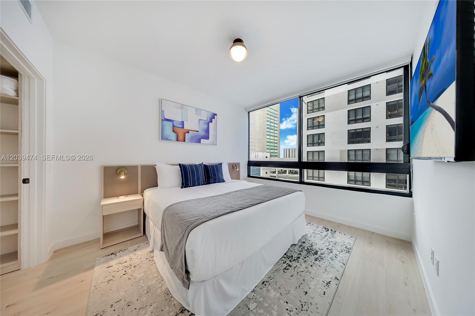A bedroom features a bed, a wall-mounted television, and a large window overlooking buildings — 225 N Miami Ave # 1510, Miami FL 33128, MIAMI, FL