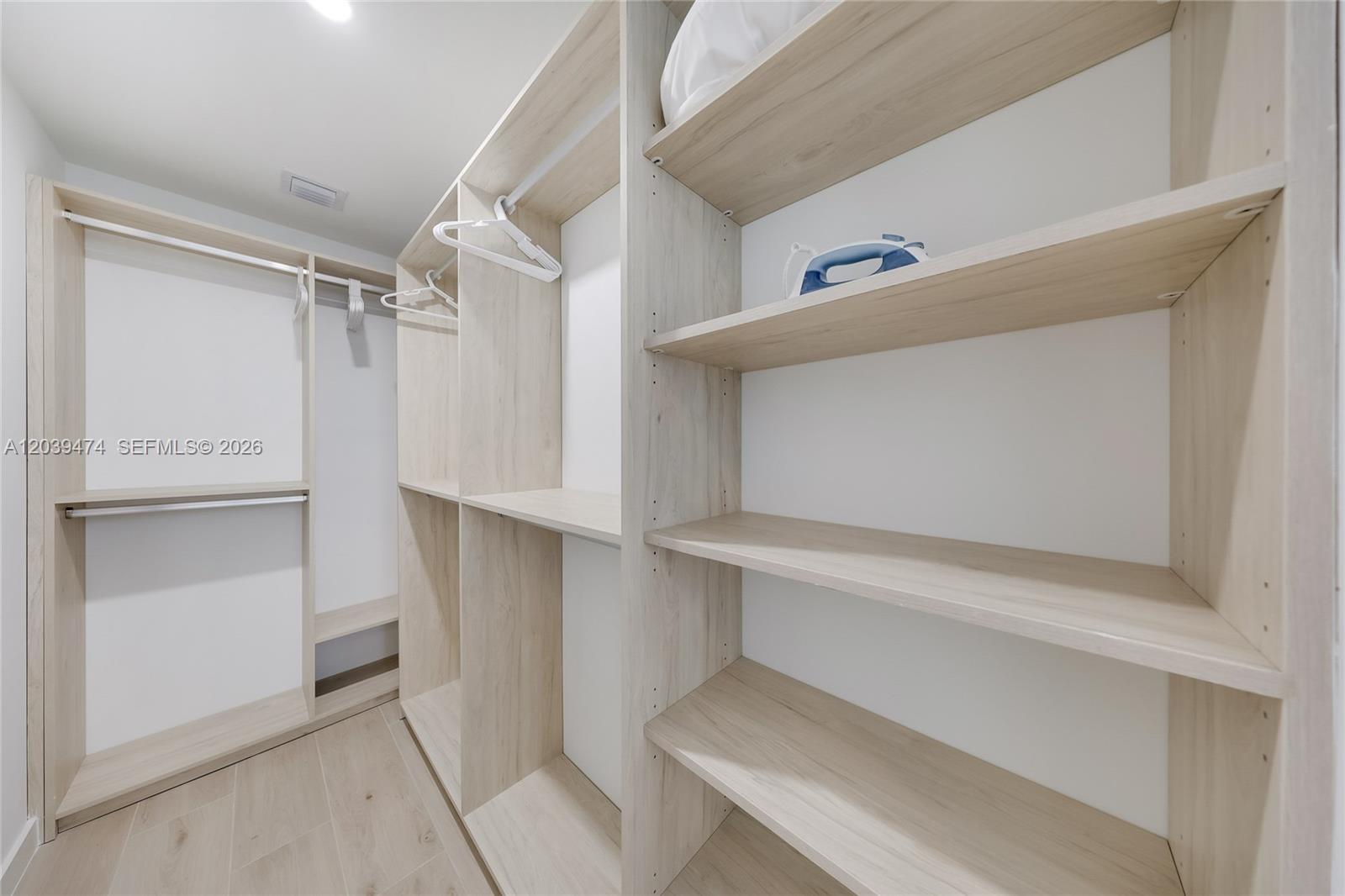 A walk-in closet features light wood-grain shelving, hanging rods, and white walls — 225 N Miami Ave # 1510, Miami FL 33128, MIAMI, FL