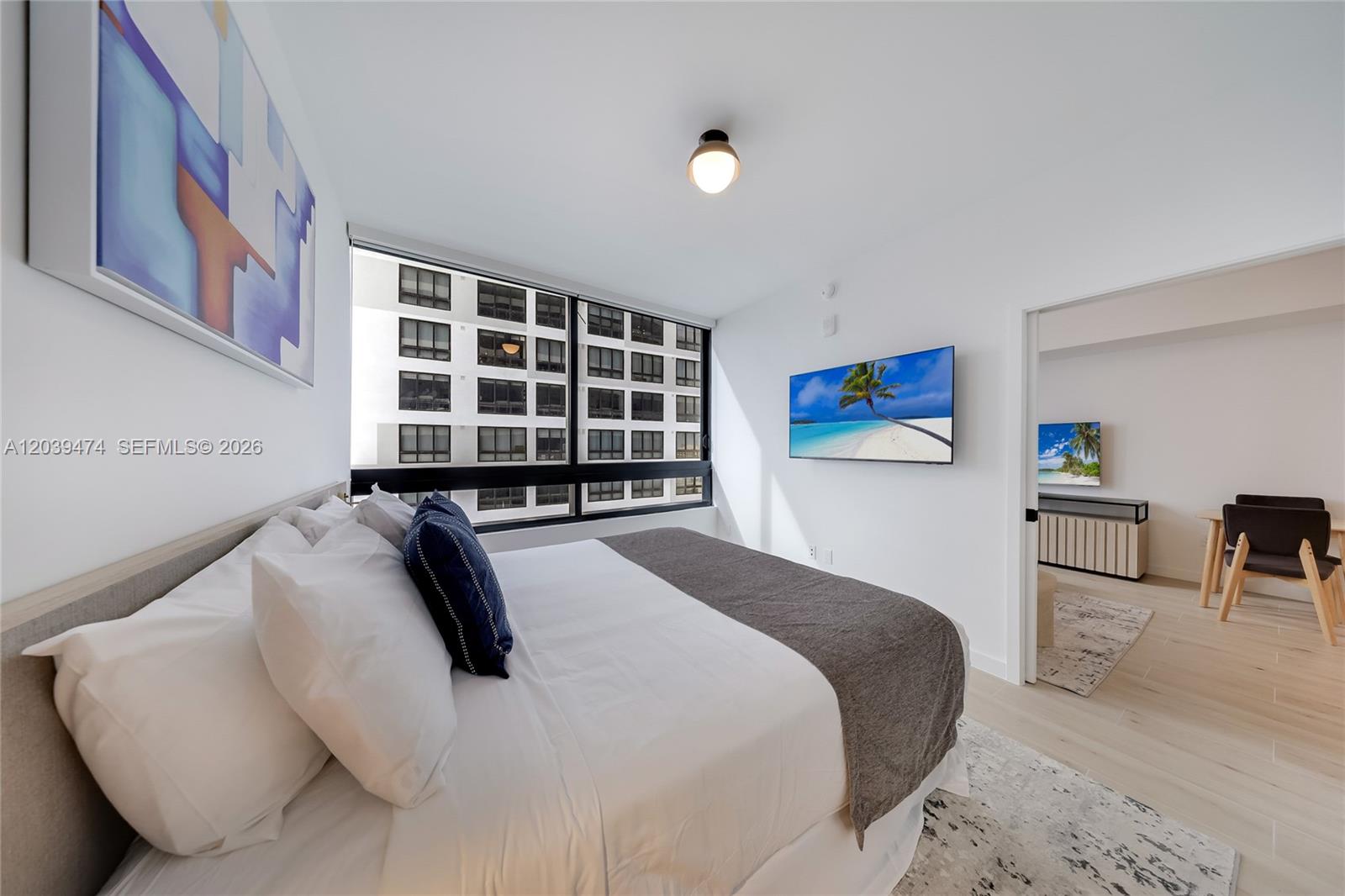 A modern bedroom features a bed, wall-mounted television, and a view of an adjacent building — 225 N Miami Ave # 1510, Miami FL 33128, MIAMI, FL