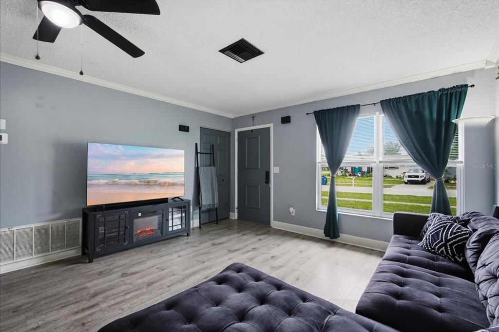 A living room features light wood-look flooring, a gray sofa, and a television on a stand — 9269 MARLER ROAD, SPRING HILL, FL