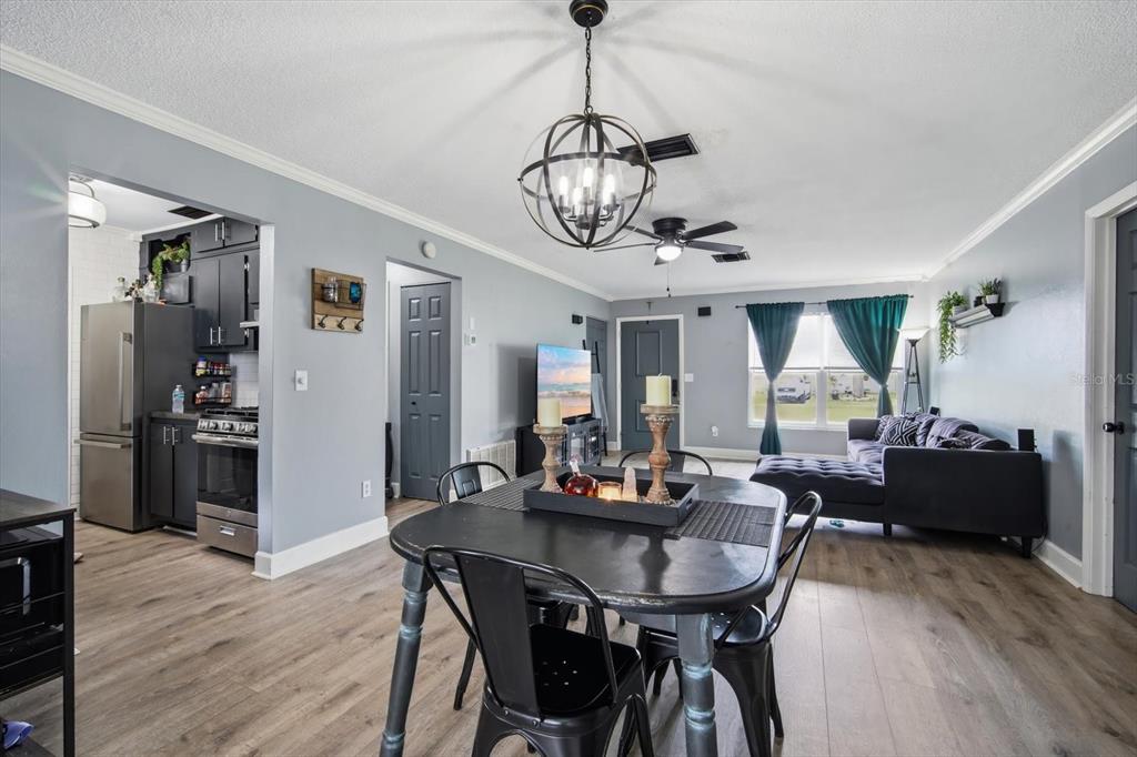 An open-concept dining and living area features gray walls, wood-look flooring, and a globe chandelier — 9269 MARLER ROAD, SPRING HILL, FL