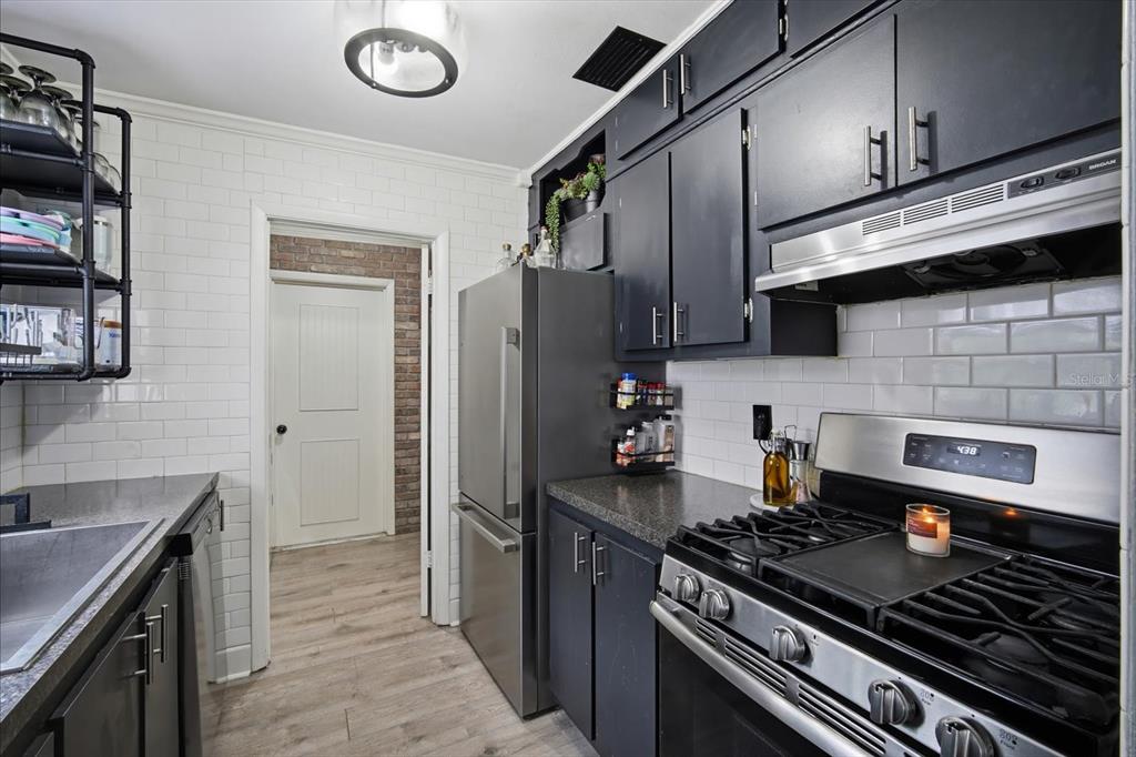 A kitchen features dark cabinets, stainless steel appliances, white subway tile walls, and wood flooring — 9269 MARLER ROAD, SPRING HILL, FL