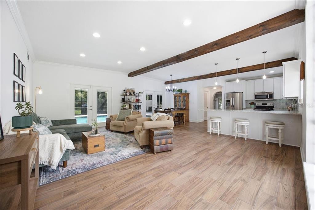 An open-concept living room and kitchen featuring wood-look tile floors and exposed ceiling beams — 1626 SIMS PLACE, LAKELAND, FL
