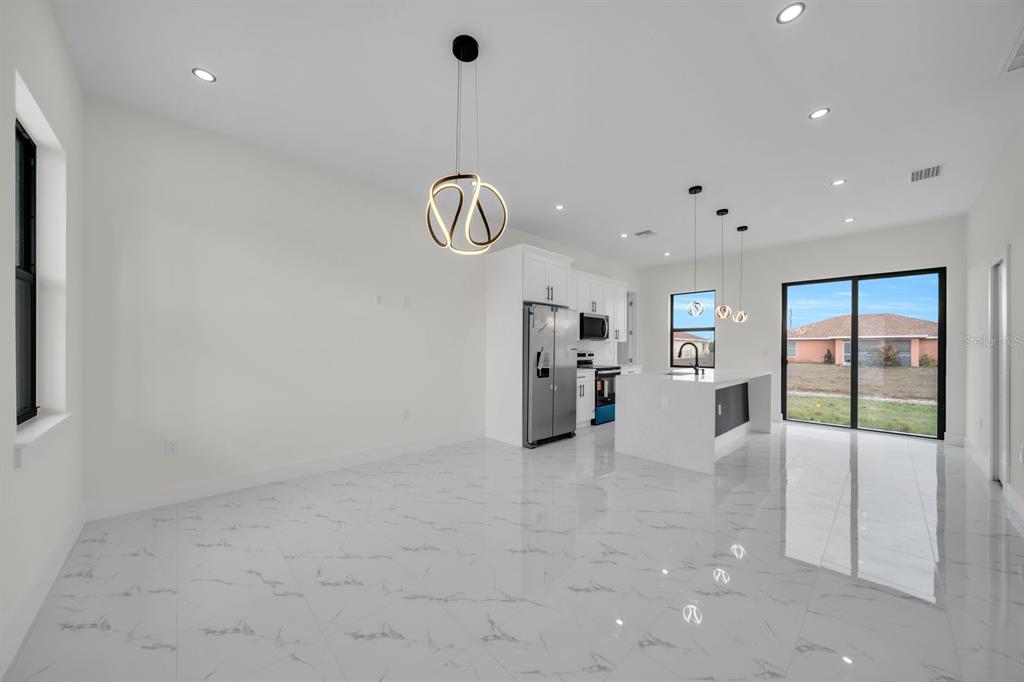 A modern open-concept kitchen and dining area with white cabinets, marble-look tile, and pendant lighting — 4003 10TH STREET SW, LEHIGH ACRES, FL