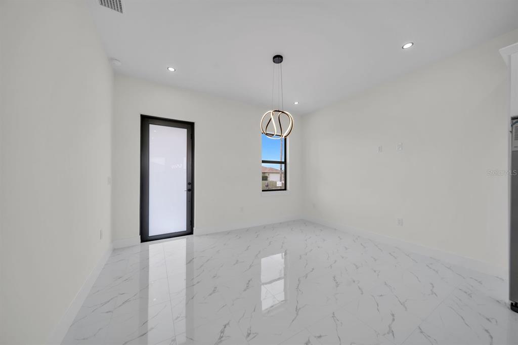 A bright, empty dining room features white marble-look tile flooring, white walls, and a modern chandelier — 4003 10TH STREET SW, LEHIGH ACRES, FL