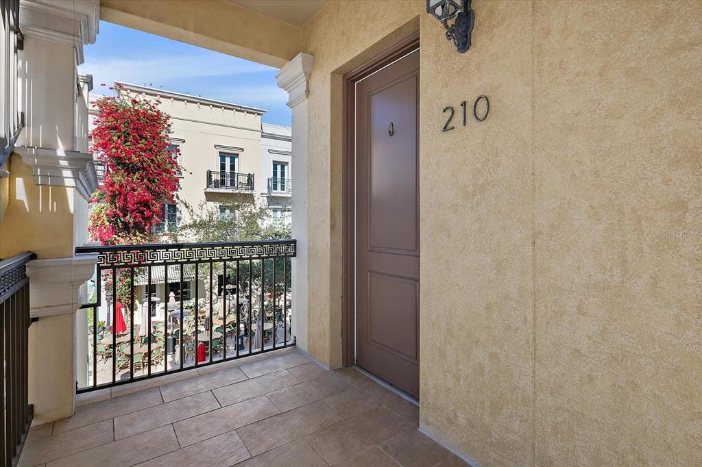 A balcony with tile flooring overlooks a courtyard with tables and a building with bougainvillea — 445 N ORANGE AVENUE UNIT 210, SARASOTA, FL
