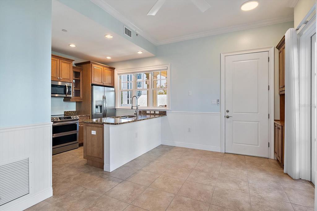 A kitchen with wood cabinets, granite countertops, and tile flooring opens to a dining area — 445 N ORANGE AVENUE UNIT 210, SARASOTA, FL