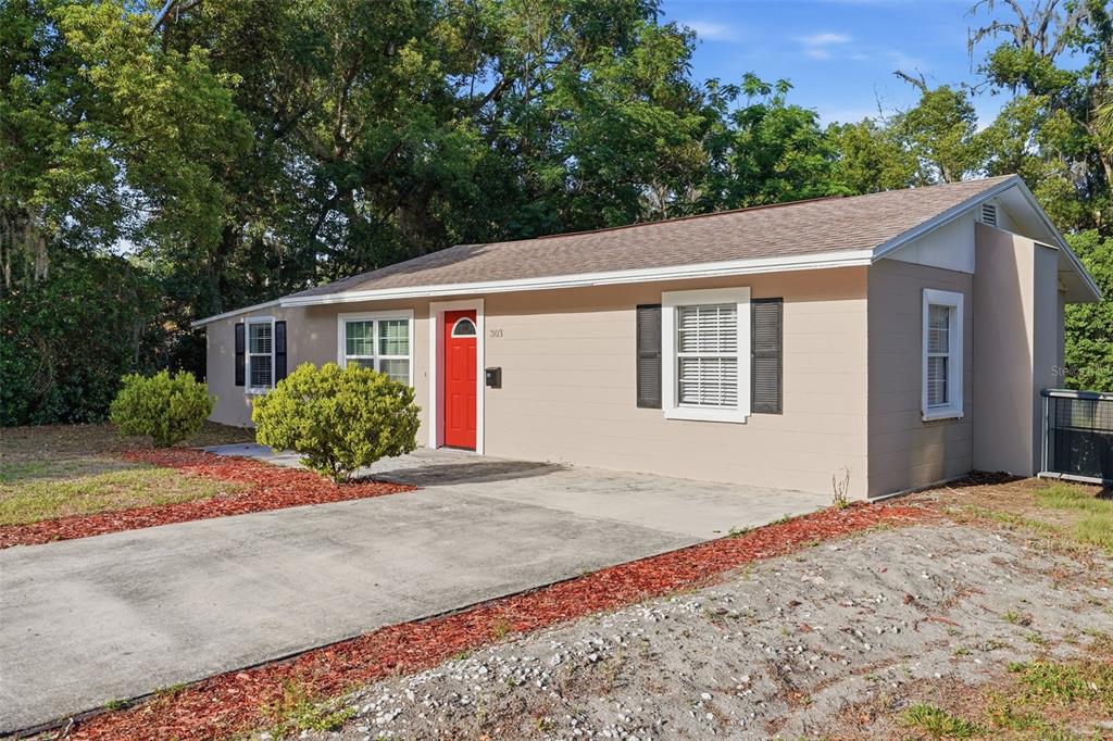 A single-story house with tan siding, a red front door, and a concrete driveway — 303 JOSEPHINE AVENUE, FRUITLAND PARK, FL