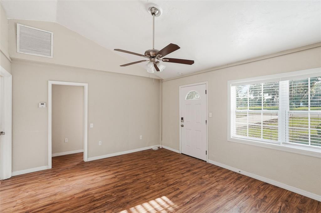 An empty room features wood-look flooring, a vaulted ceiling with a fan, and a white door — 303 JOSEPHINE AVENUE, FRUITLAND PARK, FL